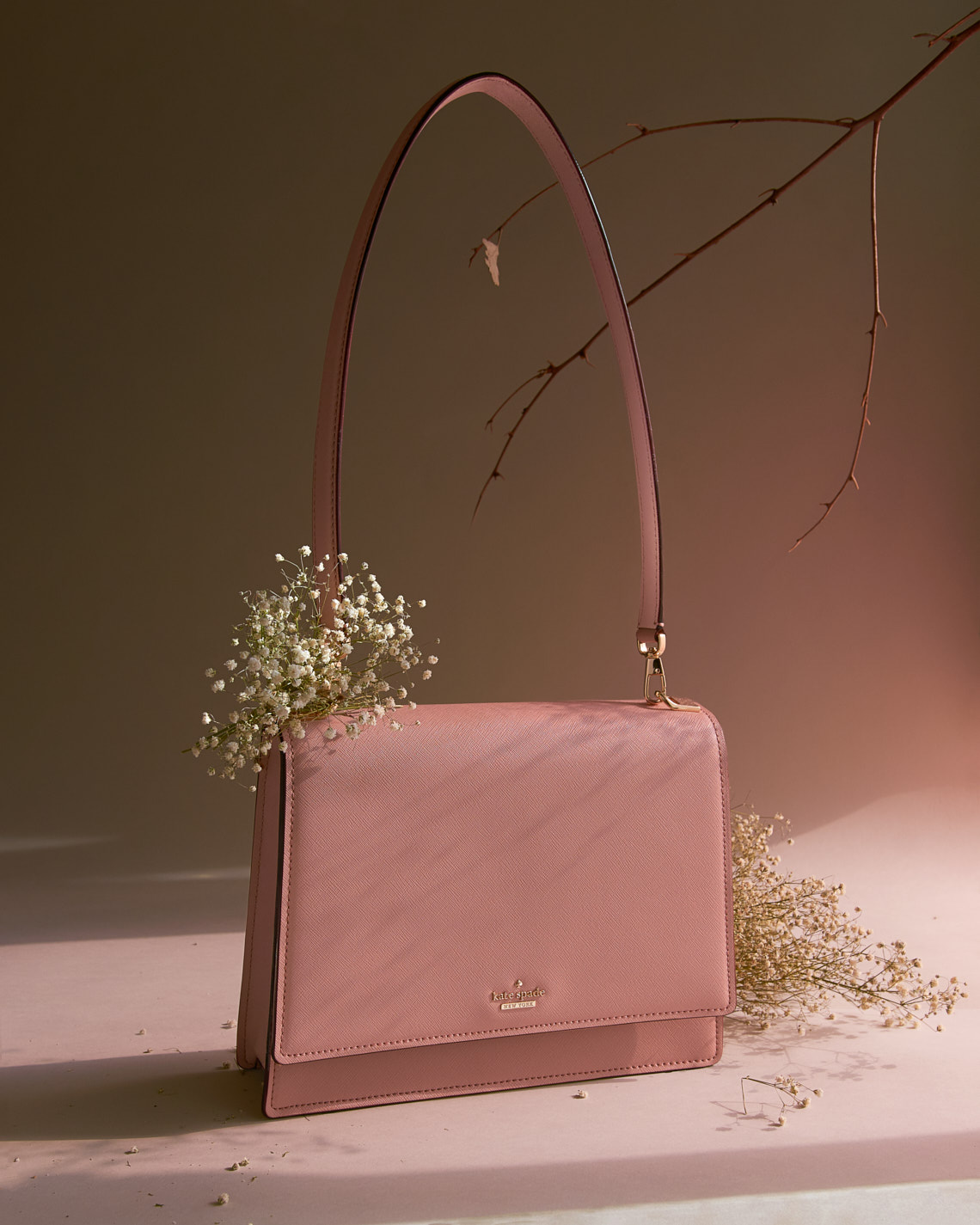 Kate Spade Pink Bag propped with wild flower lighted by window light