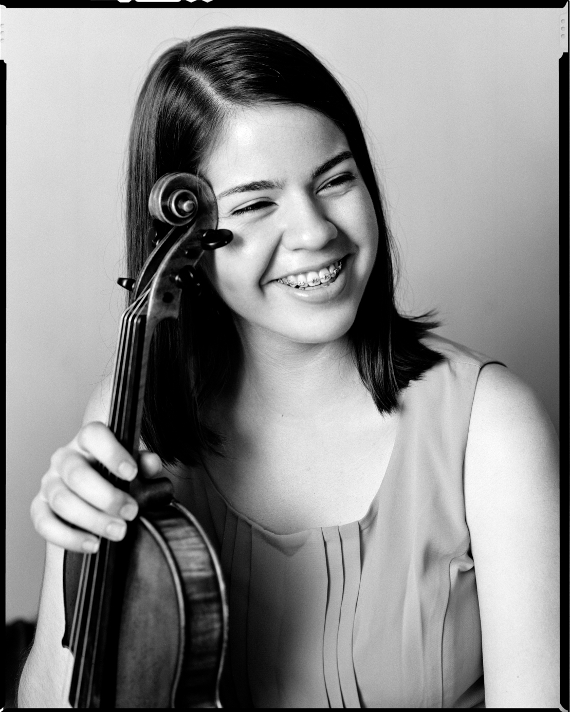 Violinist Anjelina Noh smiles with her violin leaning against her face. Photographed with 4x5 film camera.