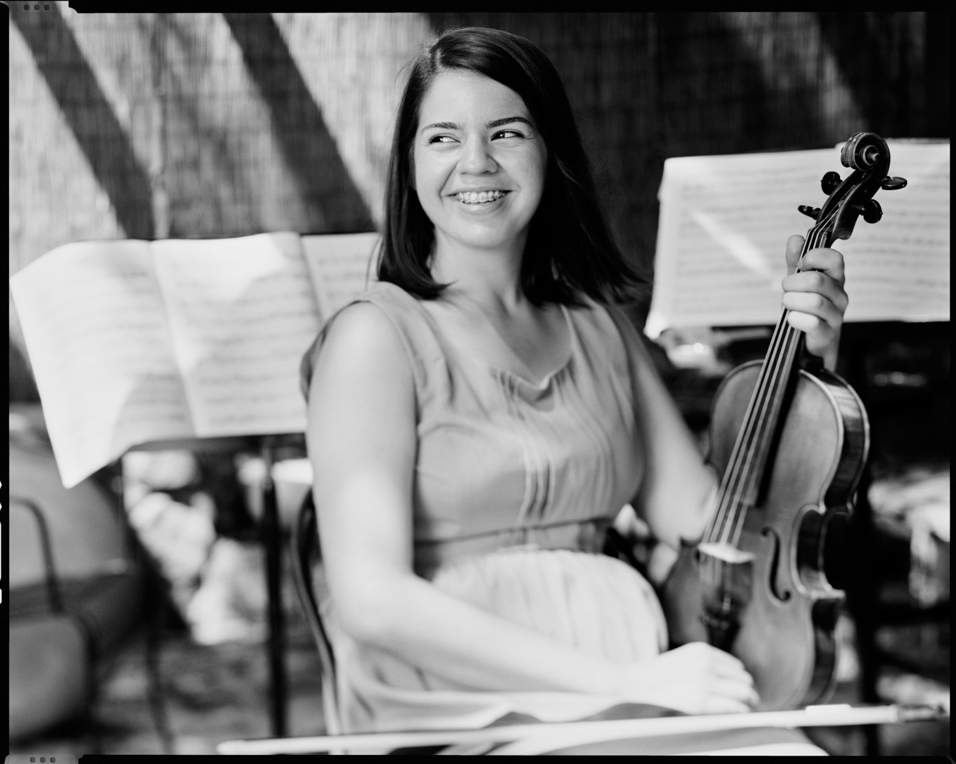 Anjelina Noh sits in front of 2 music stands in her backyard with a violin on her lap.