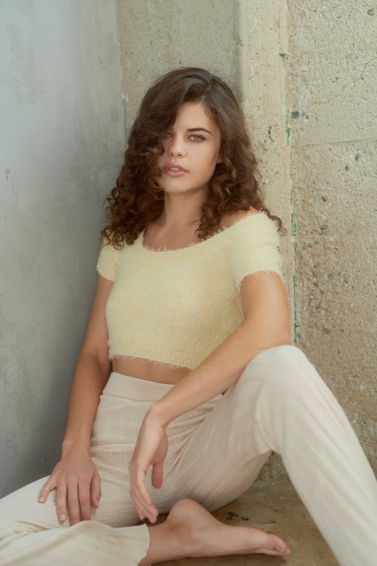 Model Kalena Audrey sits in the corner of the room with shite cropped top sweater