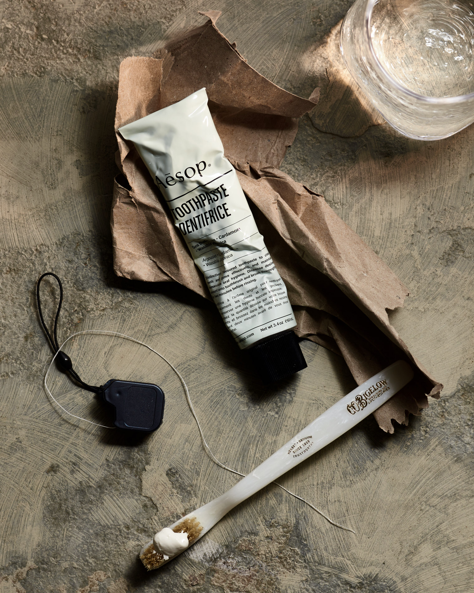 Aesop Dentifrice Toothpaste on a stone with floss and glass of water 