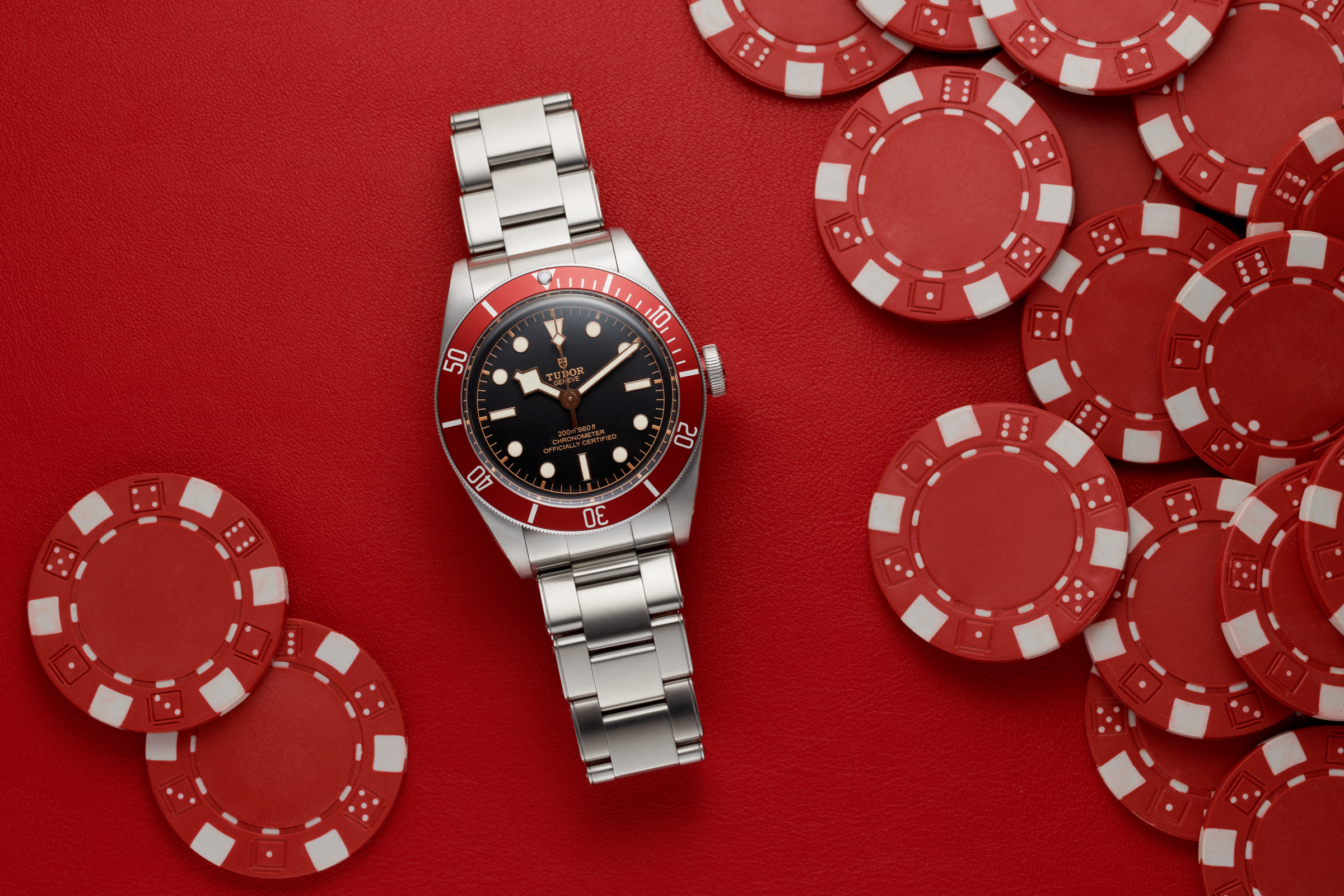 Tudor Black Bay 79230R surrounded by red poker chips on a red leather background.